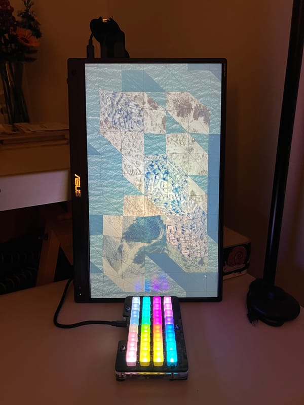 A controller with a grid of colorful buttons sits in front of a vertical monitor.
